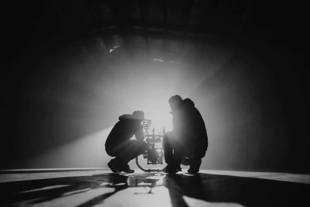 Greyscale photography of two men crouching, taking videos