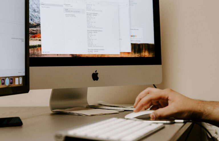 Person holding a white Apple mouse on a wooden desk