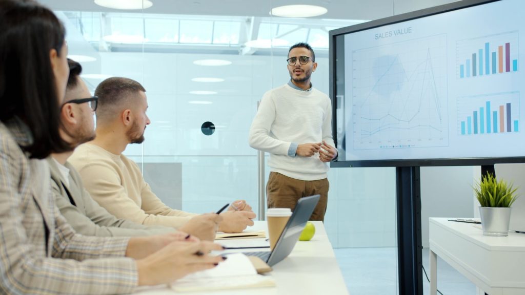 Presenter reviewing campaign results on a large screen with the team