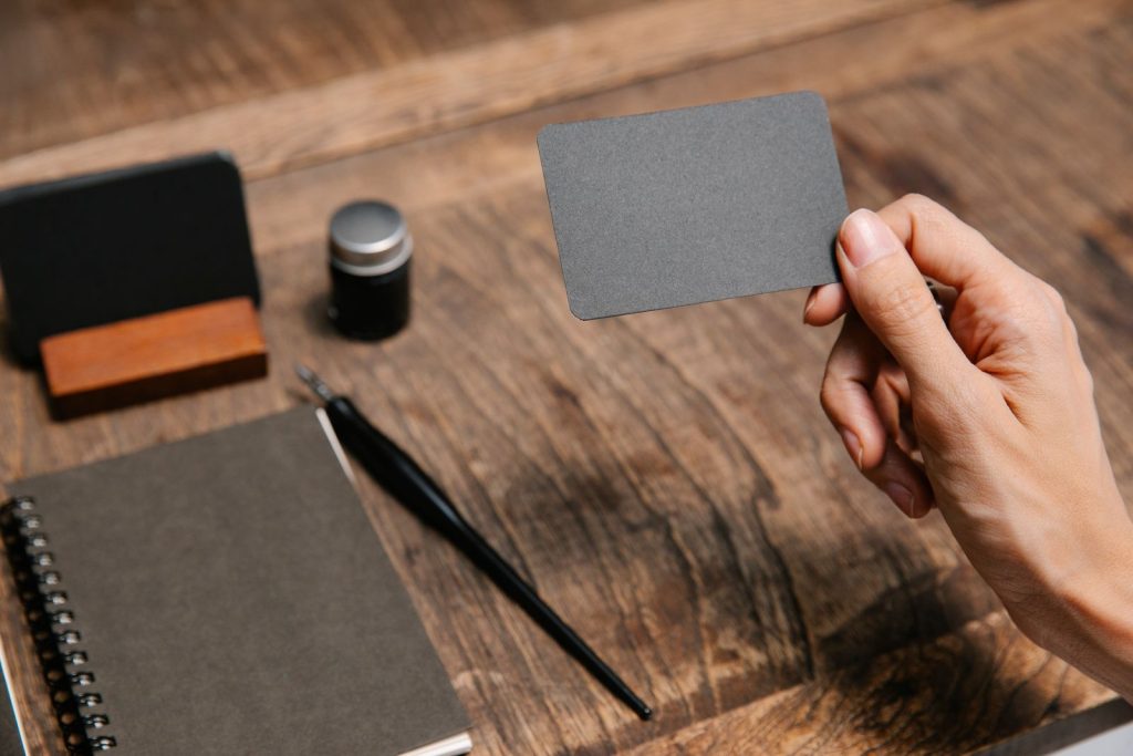 Hand holding a business card next to a notebook and pen
