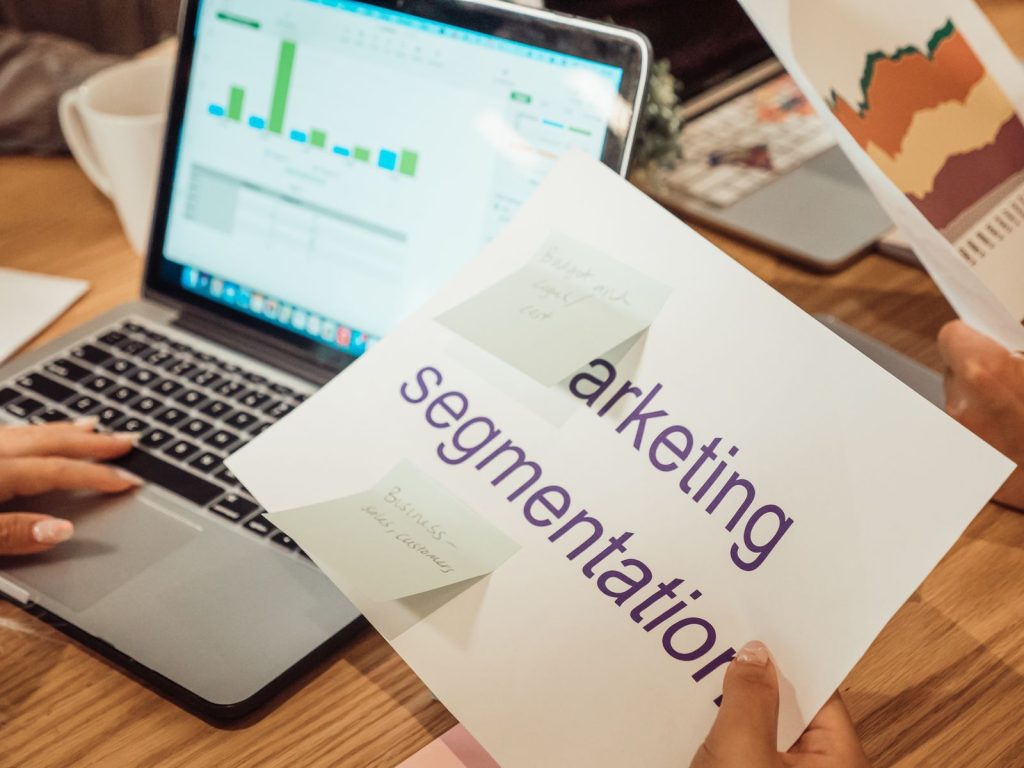 Marketing segmentation notes held over a laptop showing campaign data