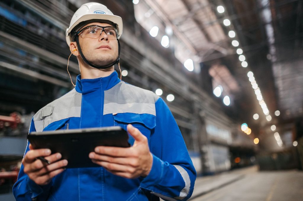 Engineer in a hard hat holding a tablet on a factory floor