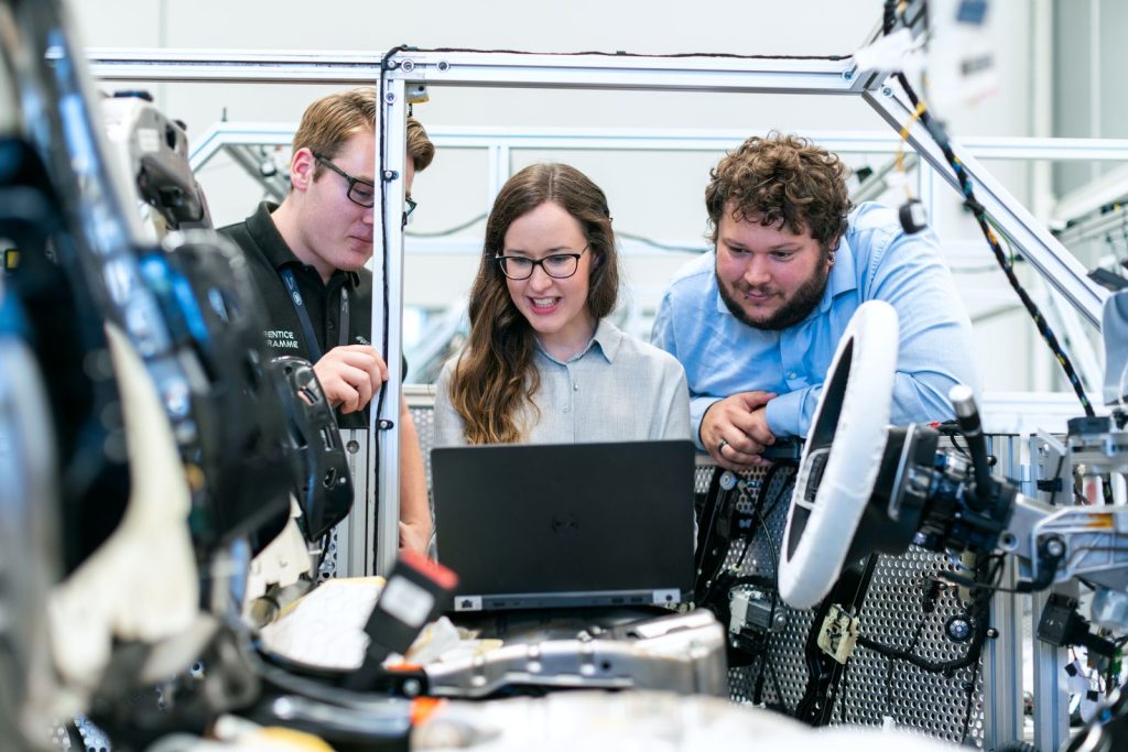 Three engineers reviewing a project on a laptop beside production equipment