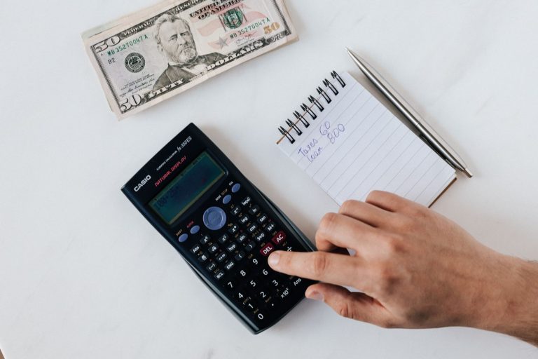 Hand using a calculator next to a notepad and cash while planning a budget