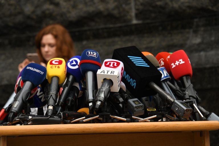 Spokesperson at a podium facing a cluster of press microphones