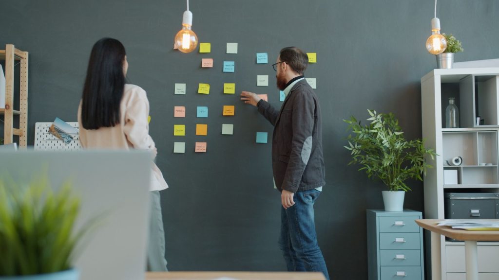Two strategists planning a campaign on a wall of sticky notes